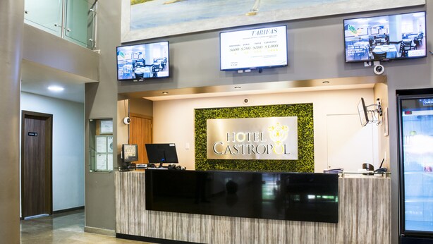 A hotel reception desk with a modern design, a digital screen displaying room rates, and a sign indicating the hotel name. - Hotel Castropol (Mexico City)