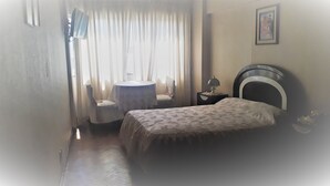 A hotel room with a bed, a round table with a chair, a lamp, and a painting on the wall. - Hotel La Joya (La Paz)