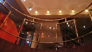 A modern interior with a central chandelier, a curved railing, and a glass elevator. - Hotel La Joya (La Paz)