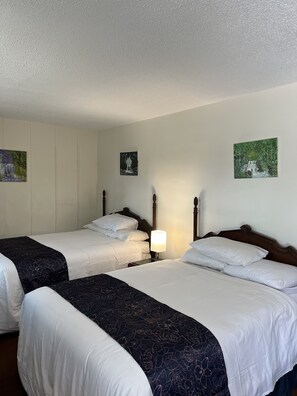 A hotel room with two single beds, a nightstand with a lamp, and two wall-mounted paintings. - Itascan Motel (Grand Rapids)