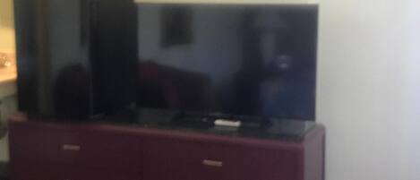 Una sala de estar con un televisor de pantalla plana sobre un mueble oscuro, un microondas encima y un sofá rojo.