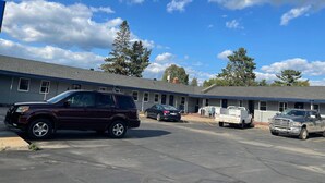 A motel with a row of rooms, a parking lot, and a clear blue sky with clouds. - Itascan Motel (Grand Rapids)