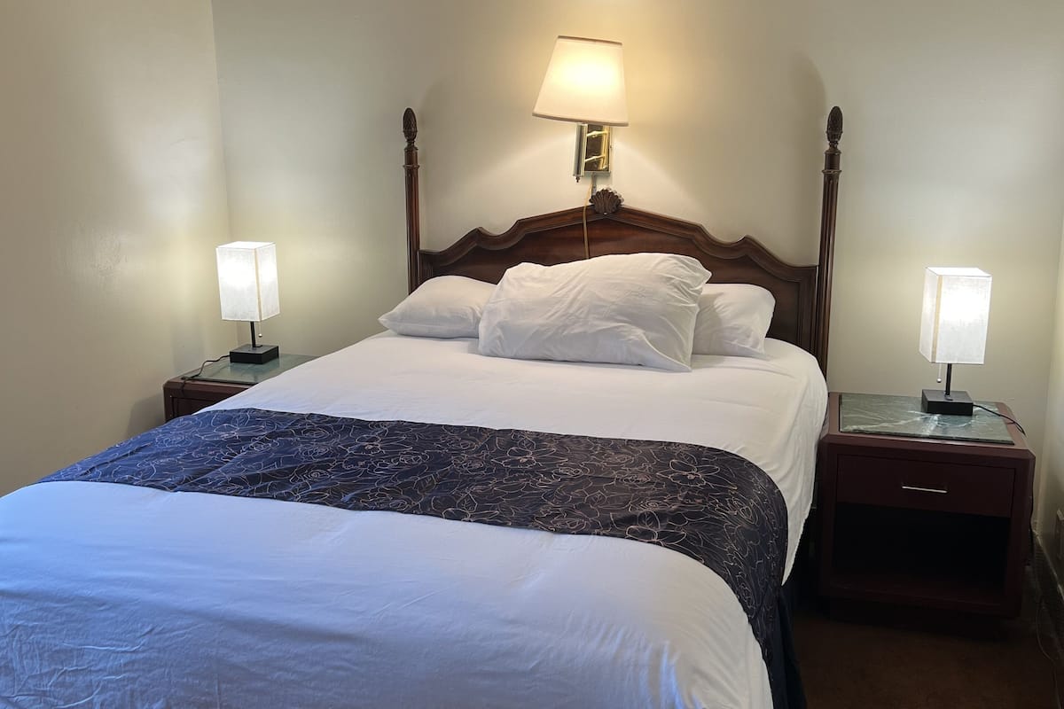 A neatly made bed with white and blue bedding, two bedside lamps, and a wooden headboard.