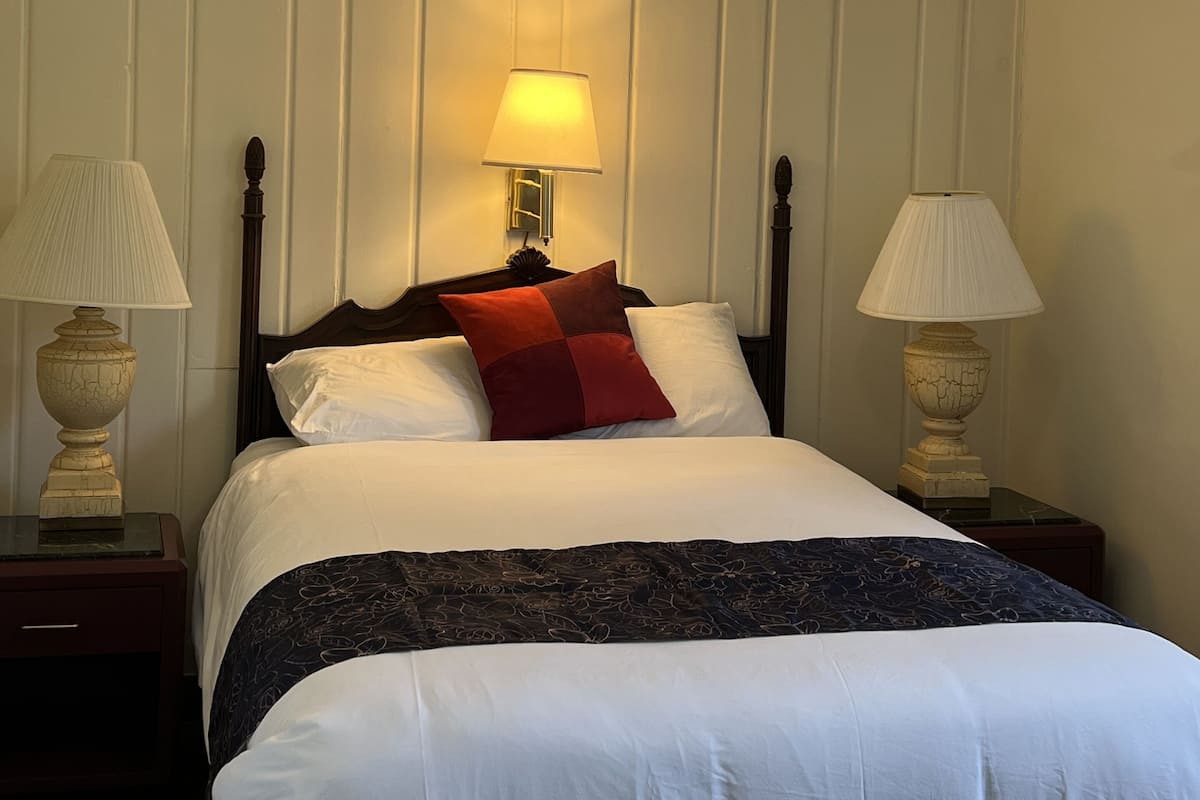 A neatly made bed with white linens and a red accent pillow, flanked by two bedside lamps on matching nightstands.