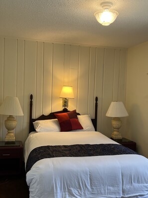 A neatly made bed with white linens and a red accent pillow, flanked by two bedside lamps on matching nightstands. - Itascan Motel (Grand Rapids)