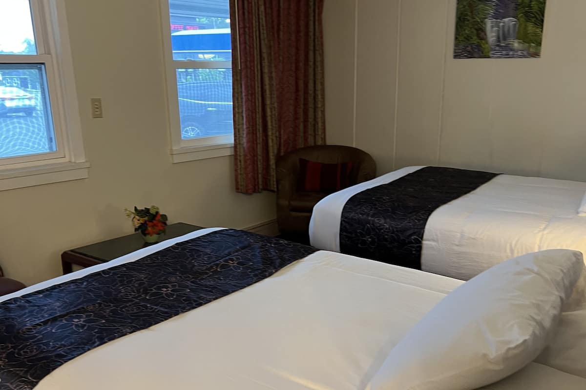 A hotel room with two beds, a chair, a window with curtains, and a painting on the wall.