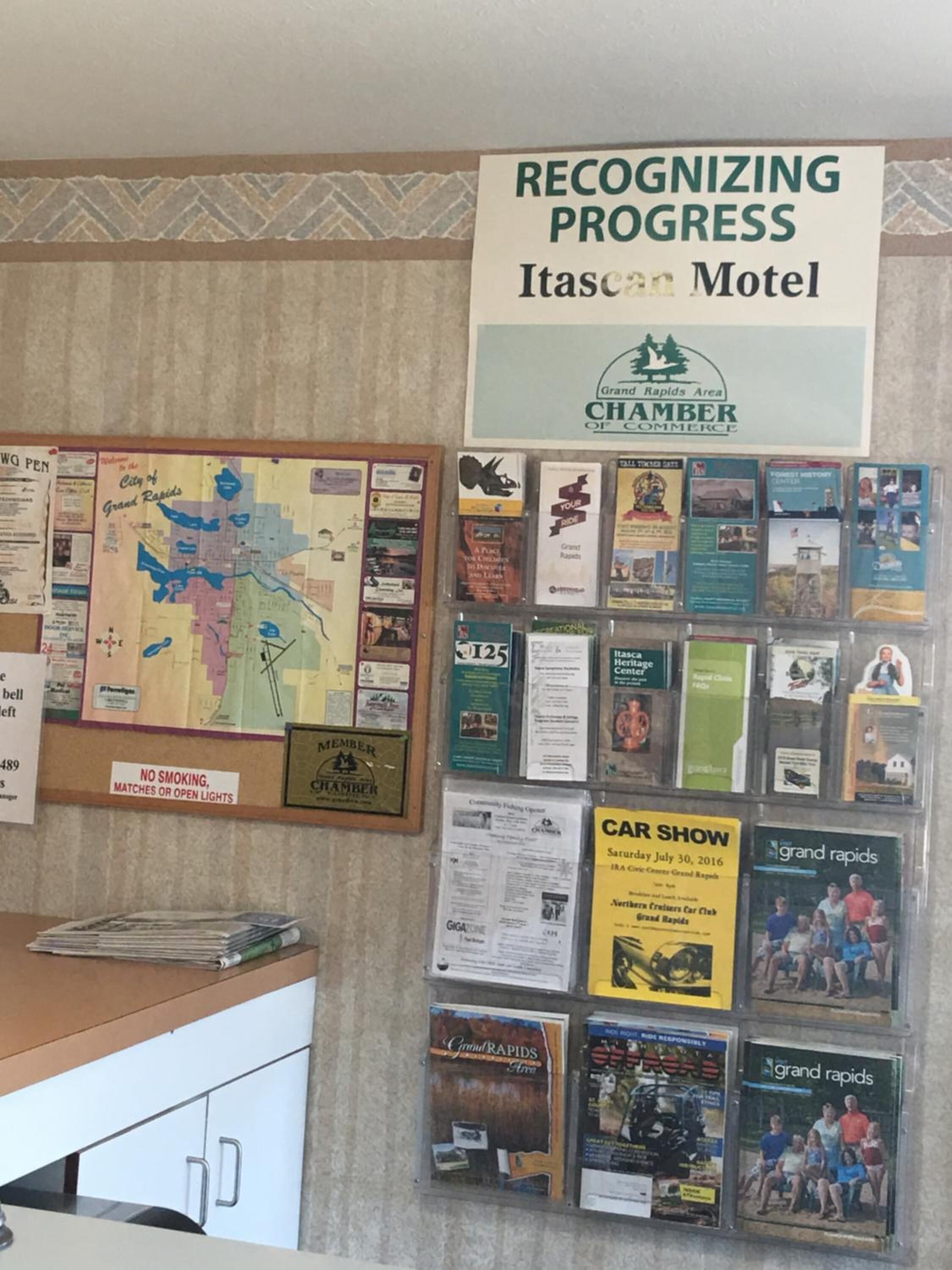 Una pared con varios carteles informativos y un mapa, incluyendo un cartel que dice 'Recognizing Progress' para el Itasca Motel.