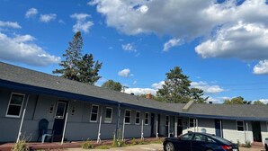 A motel with a row of rooms, a covered parking area, and a clear blue sky with clouds. - Itascan Motel (Grand Rapids)