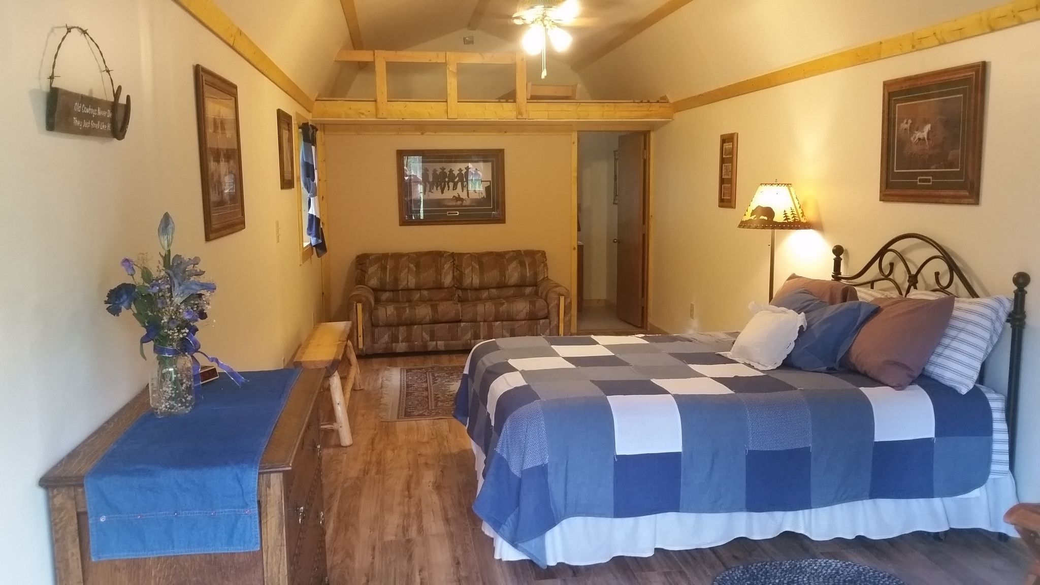 A cozy bedroom with a checkered bedspread, a wooden bench, a vase of flowers, and a rustic wall decor.