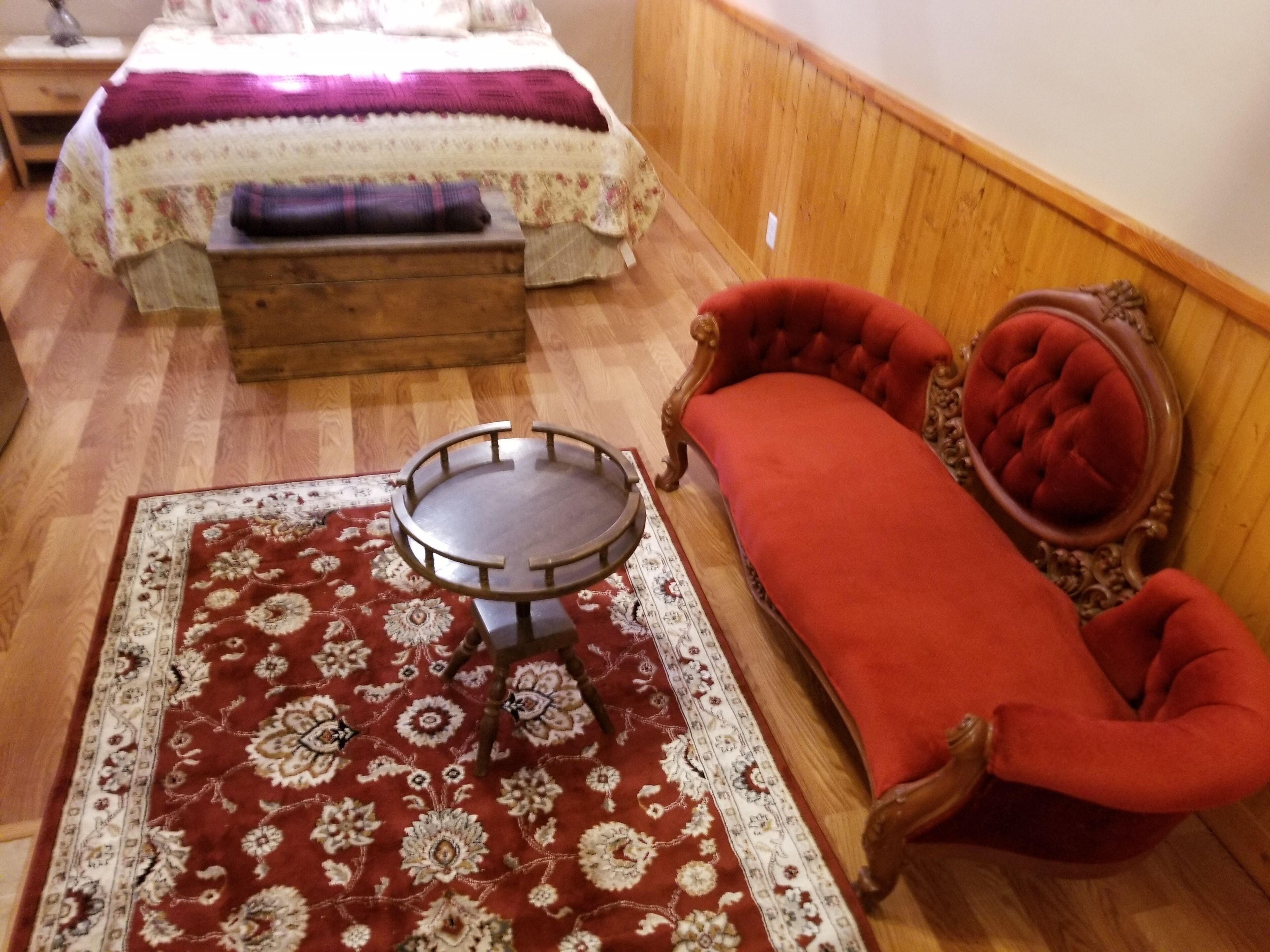 Une pièce comprenant un lit, un canapé rouge, une petite table ronde et un tapis à motifs.