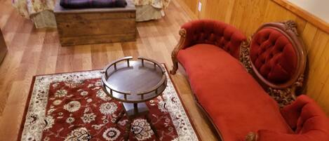Une pièce comprenant un lit, un canapé rouge, une petite table ronde et un tapis à motifs.
