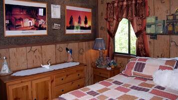 A bedroom with a wooden dresser, a bed with a quilt, a nightstand with a lamp, and a window with curtains.