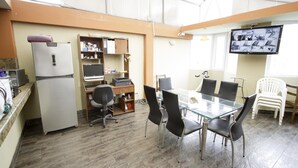 A conference room with a glass table, black chairs, a white refrigerator, a wooden cabinet, and a television mounted on the wall.
