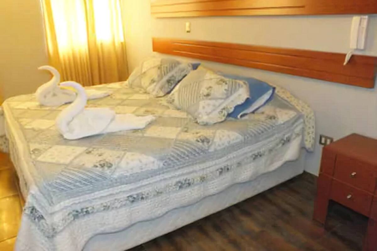 A hotel room with a bed, wooden headboard, and a small red cabinet.