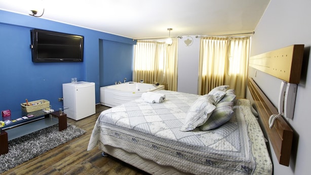 A hotel room with a large bed, a bathtub, a flat-screen TV, a small desk, and a window with curtains.