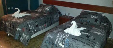 Dos camas con ropa de cama estampada y almohadas con forma de cisne, un cabecero de madera y piso de baldosas.