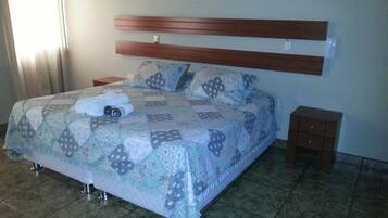 Un dormitorio con una cama, cabecera de madera, dos mesitas de noche y suelo de baldosas.