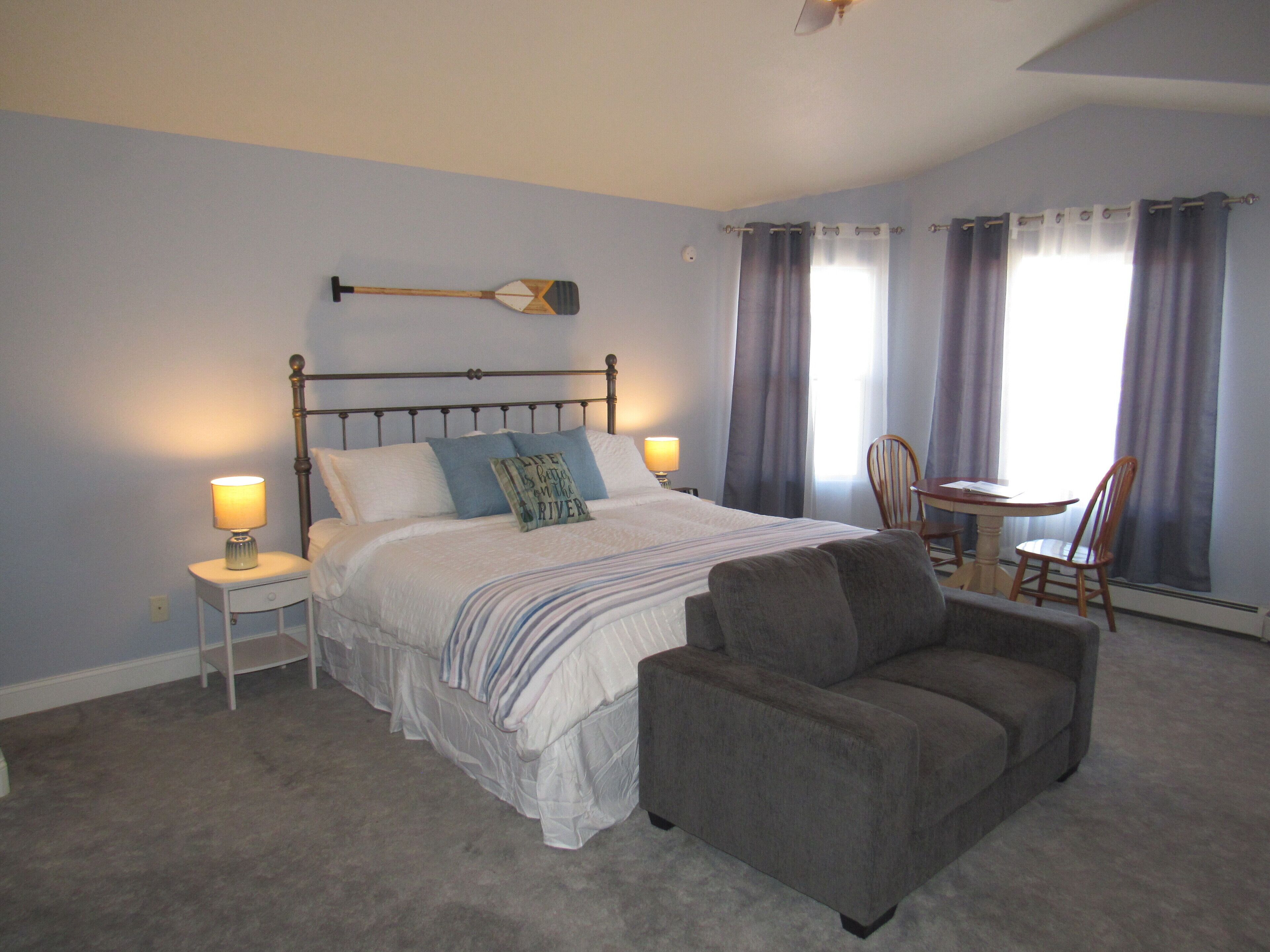 A bedroom with a bed, bedside lamps, a chair, and a dining table.