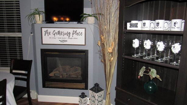A living room with a fireplace, a television, and a shelf with decorative items. - Castle Creek B&B (Grand Junction)