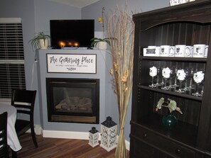 A living room with a fireplace, a television, and a shelf with decorative items. - Castle Creek B&B (Grand Junction)