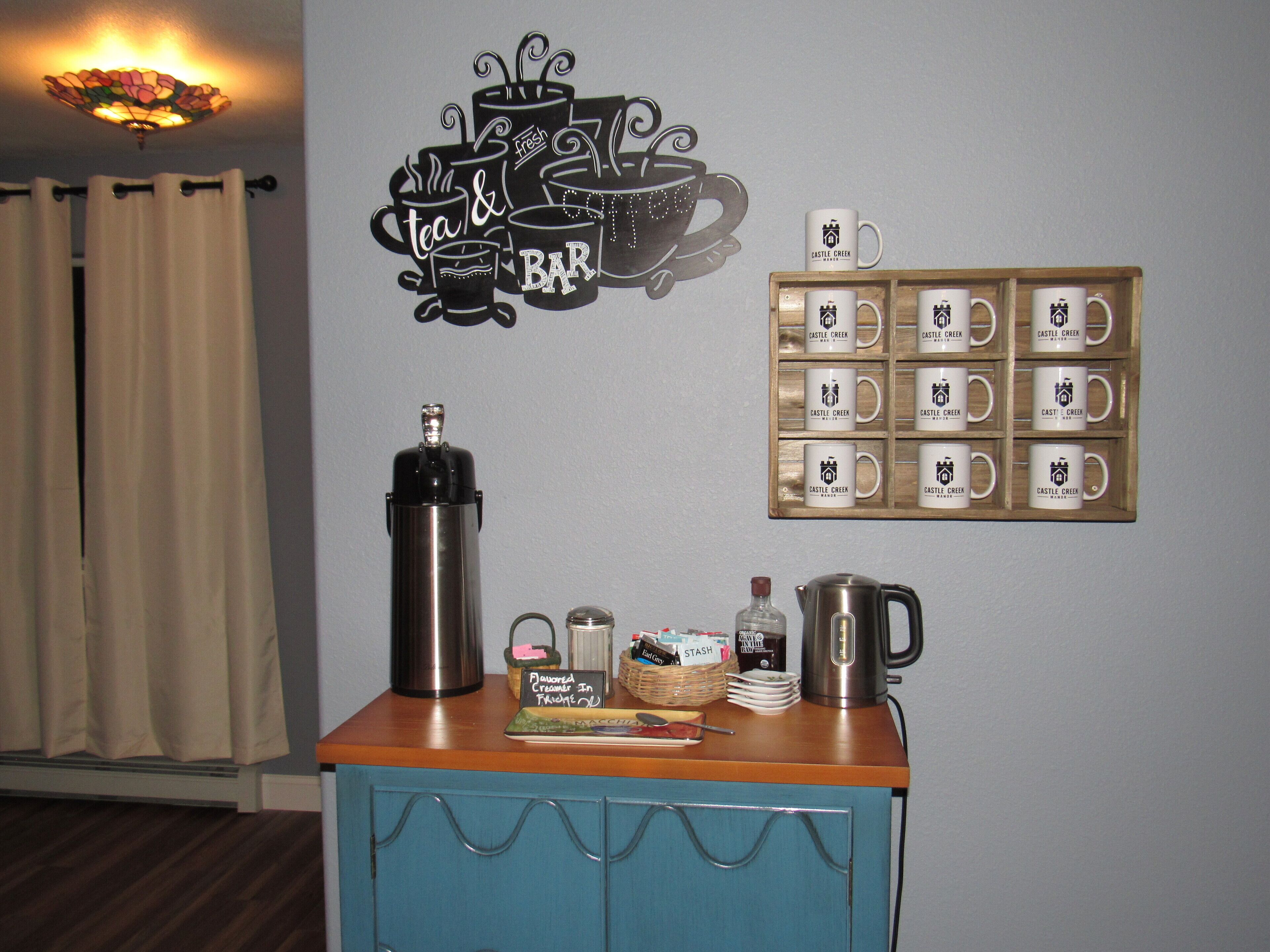 A coffee station with a coffee pot, a thermos, and a mug display on a wall.