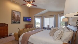 A bedroom with a large bed, a ceiling fan, a television, and a window with curtains. - Castle Creek B&B (Grand Junction)