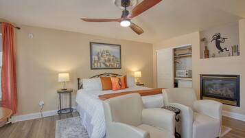 A hotel room with a bed, two bedside lamps, a ceiling fan, a painting on the wall, a microwave, and a television.