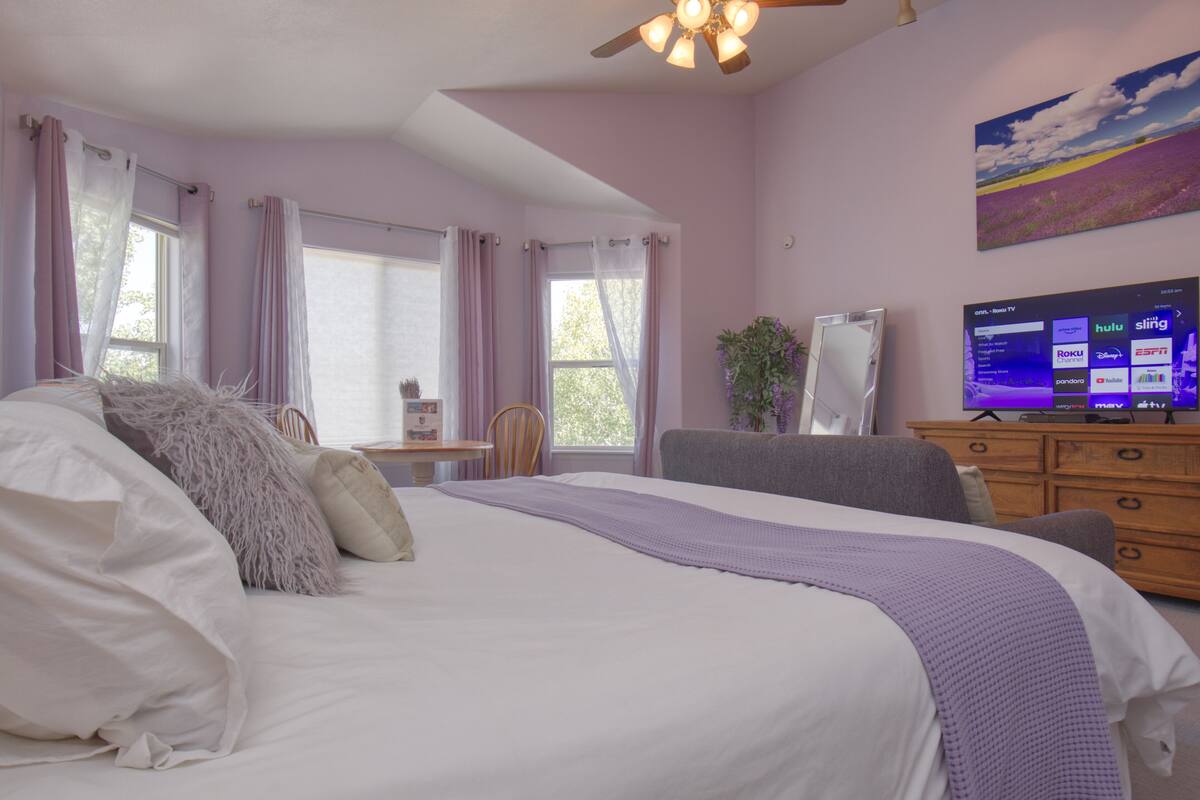 A bedroom with a large bed, a desk, a chair, a TV, and a window with curtains.