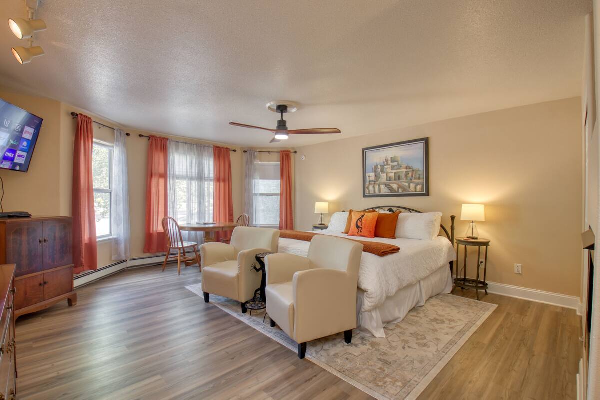 A hotel room with a bed, two armchairs, a desk, and a television.