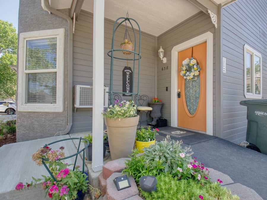 A house with a porch, a welcome sign, a door with a floral wreath, and a trash can.