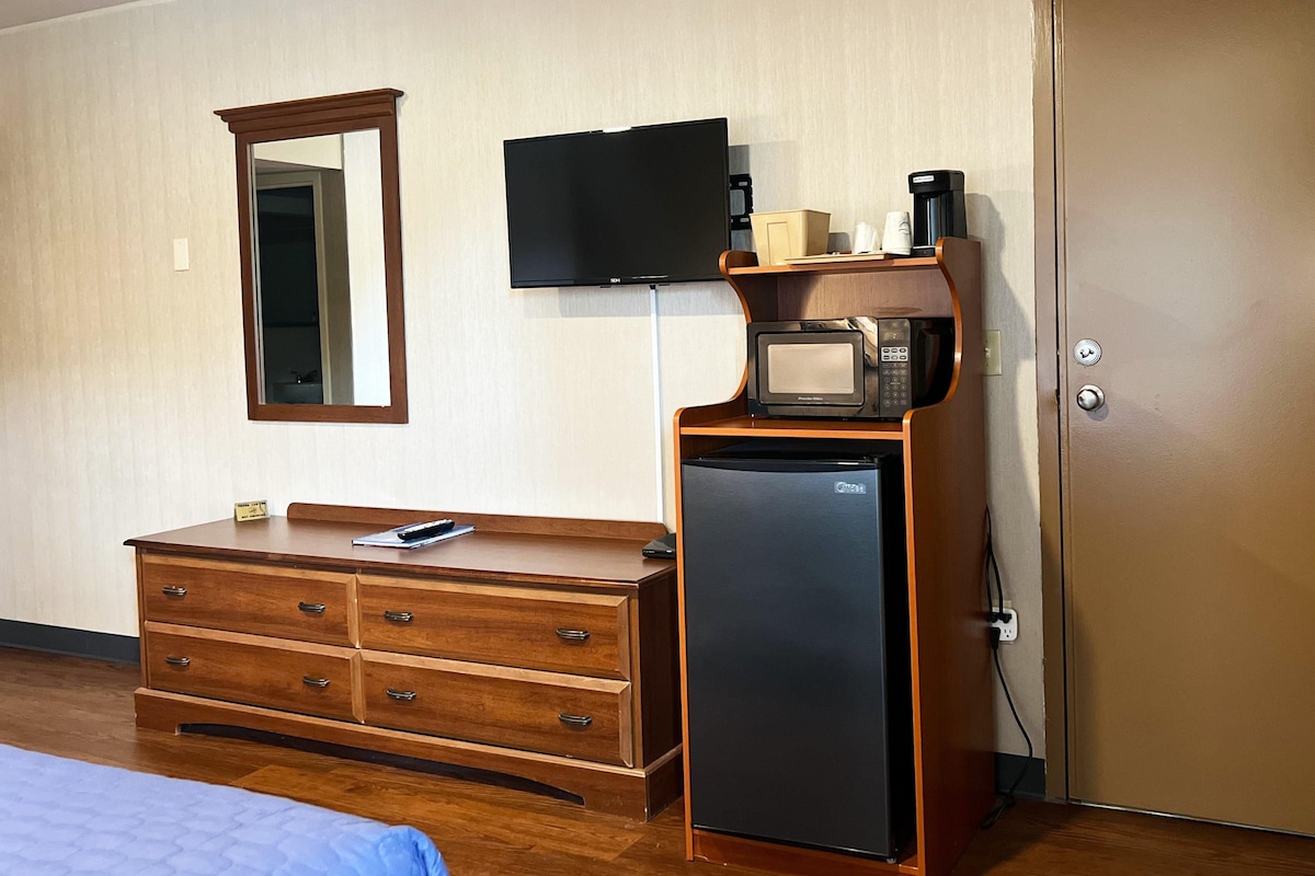 Ein Hotelzimmer mit einem Holzkleiderschrank, einem an der Wand montierten Fernseher, einer Mikrowelle und einem Kühlschrank.