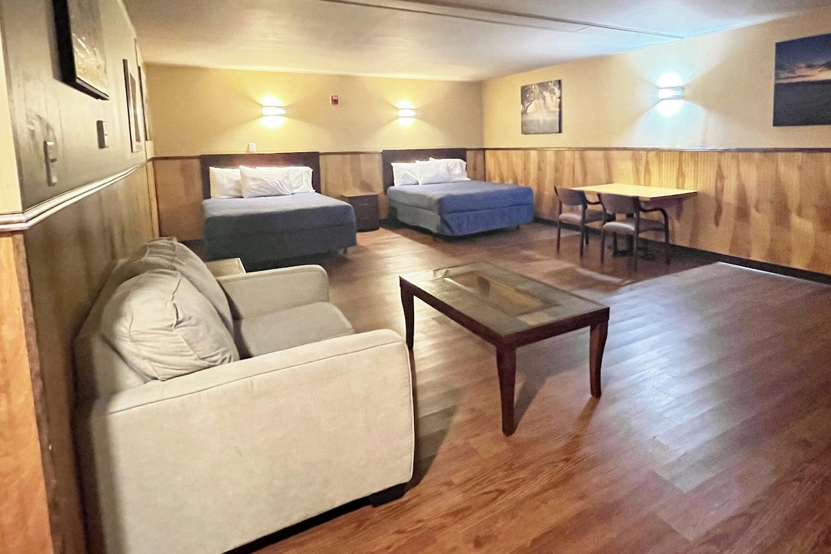 Hotellihuone, jossa on sohva, kaksi erillistä sänkyä, pieni pöytä ja ruokailutila tuoleineen.