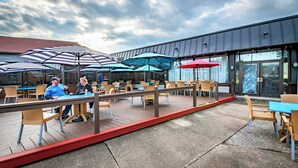 Ein Außenbereich mit Tischen, Stühlen, Sonnenschirmen und einer Holzterrasse.