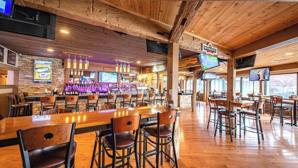Eine Bar mit Holzboden und -wänden, Barhocker und einem Fernsehbildschirm.