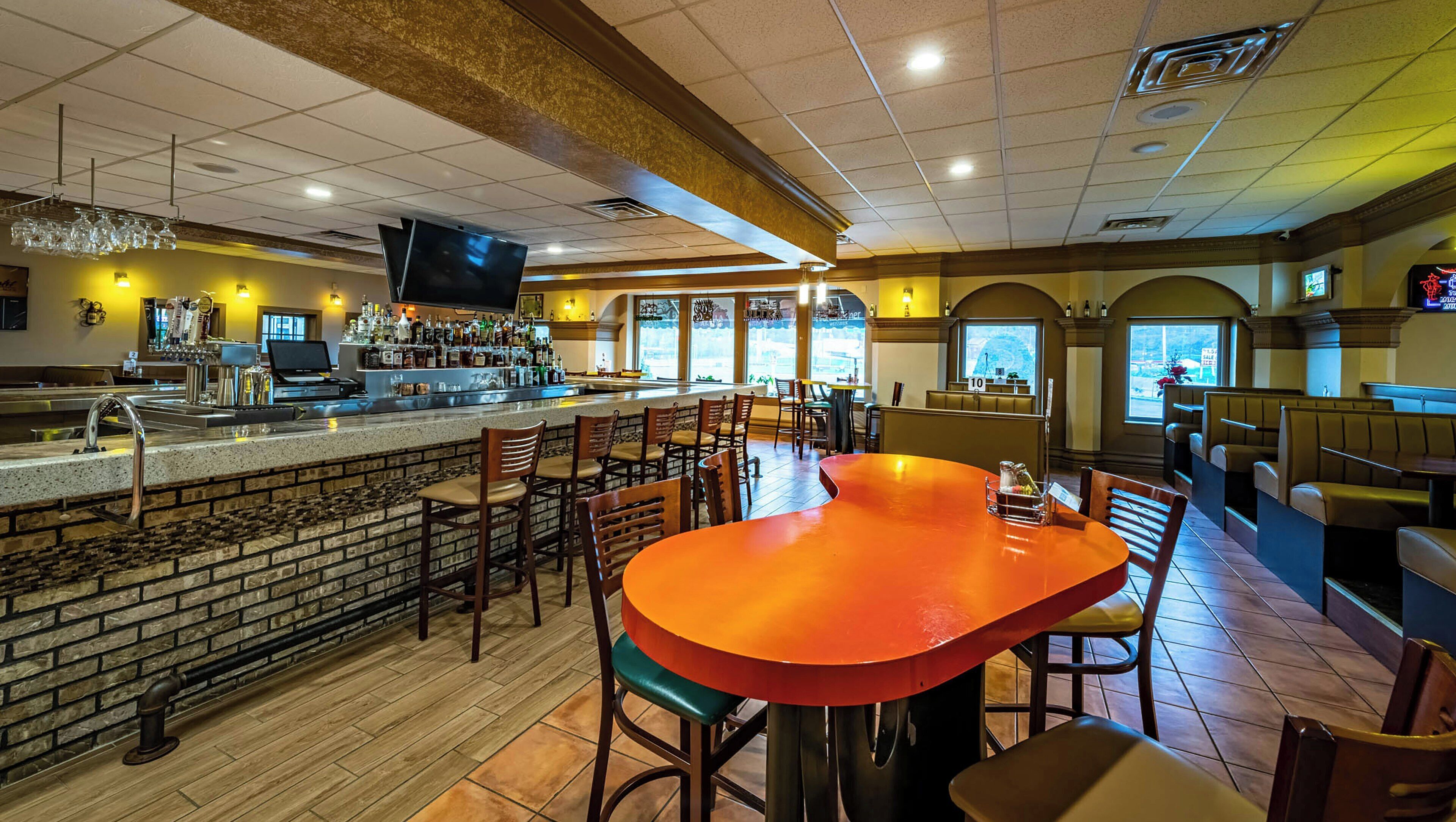 A bar area with a brick counter, multiple seating options, and a television mounted on the wall.