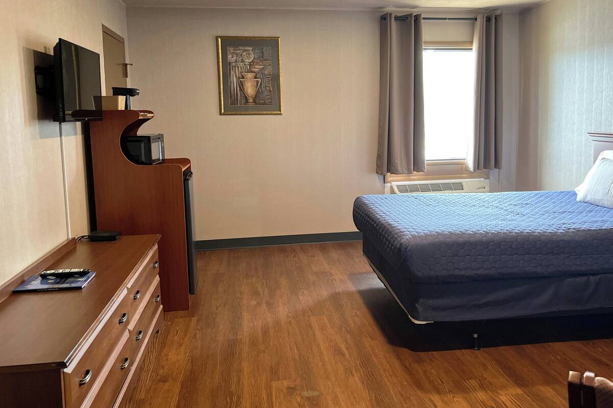 Hotellihuone, jossa on sänky, työpöytä, tuoli, televisio ja taulu seinällä.