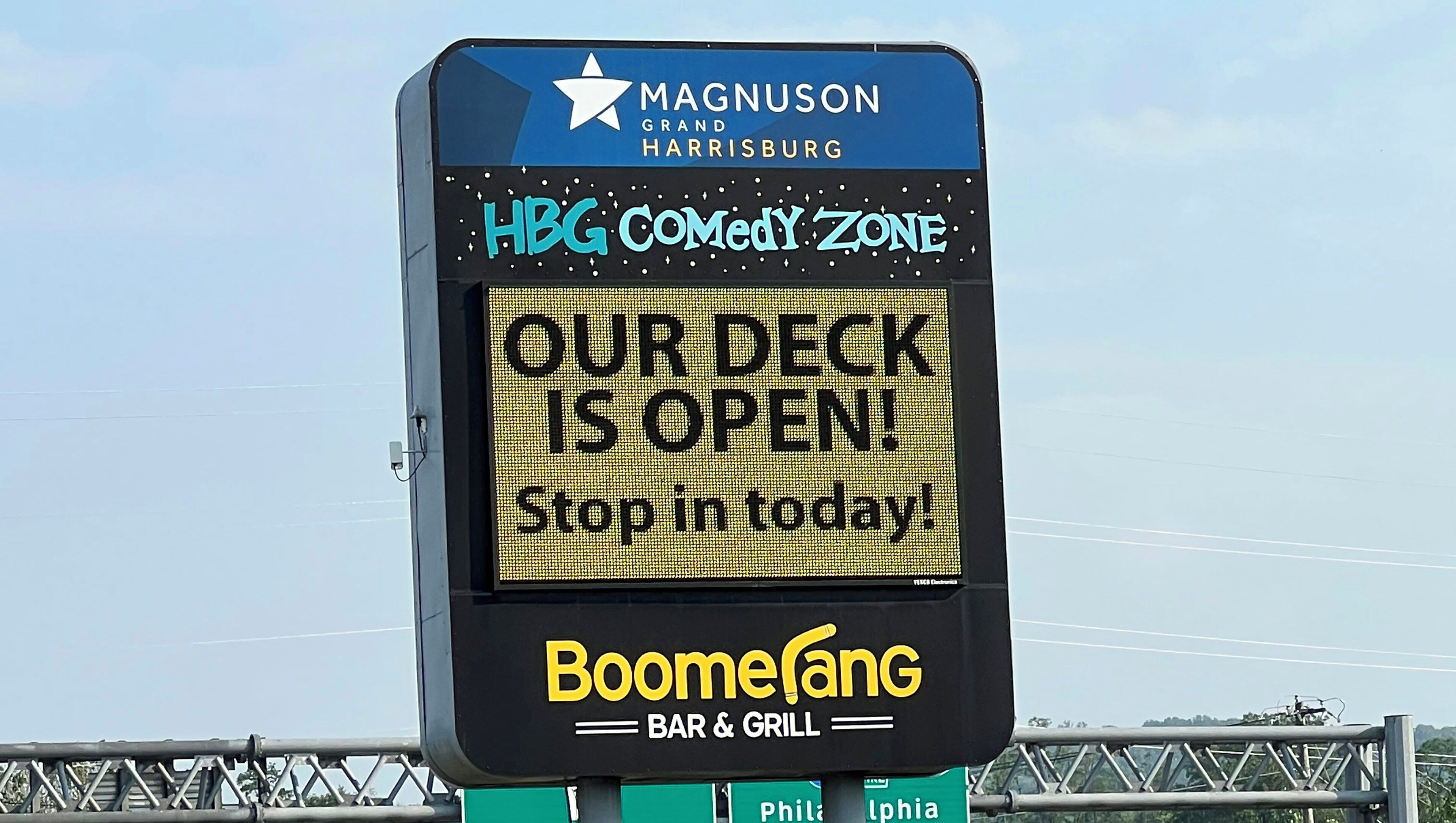 A digital signboard advertising a comedy zone and a deck opening, with a Boomefang bar and grill below.