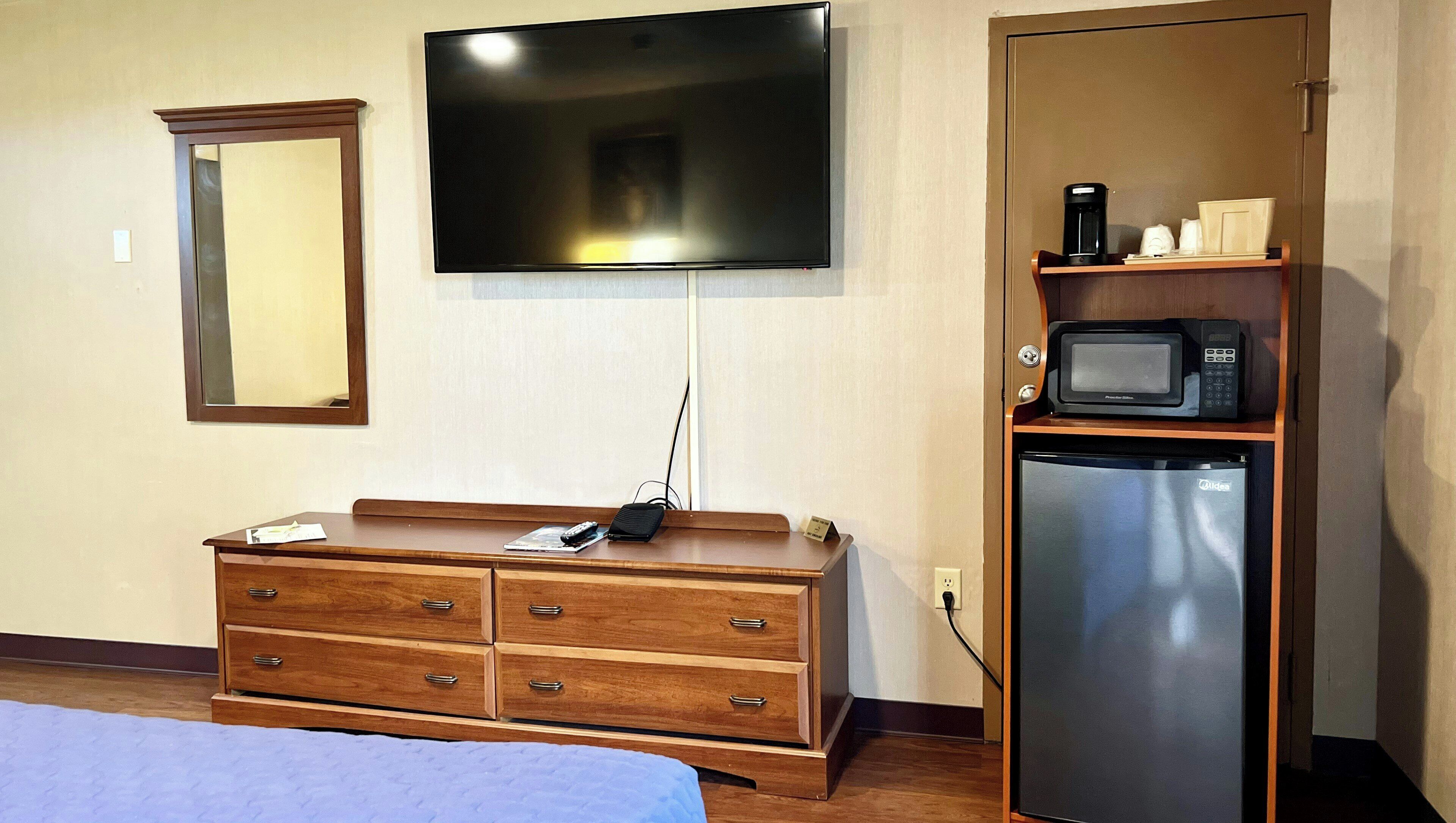 Ein Hotelzimmer mit einem Holzkoffer, einem flachbildfernseher an der Wand, einer Mikrowelle und einem Kühlschrank.