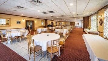 A banquet hall with round tables and chairs, a tiled floor, and a patterned wall.