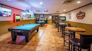 Ein Billardraum mit Billardtischen, einer Bar und Fernsehern, die Sport zeigen.