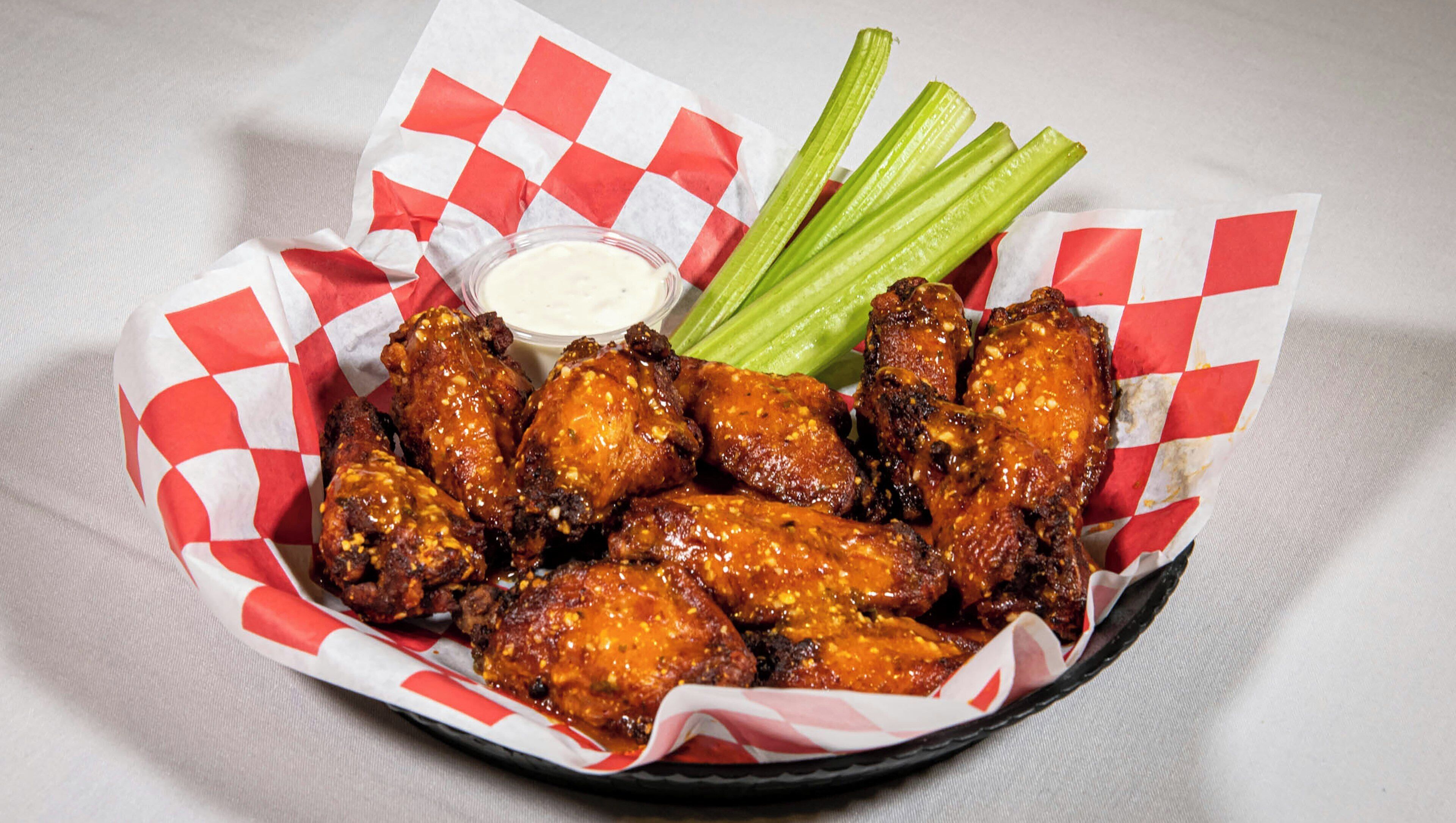 A basket of chicken wings with celery and a dipping sauce.