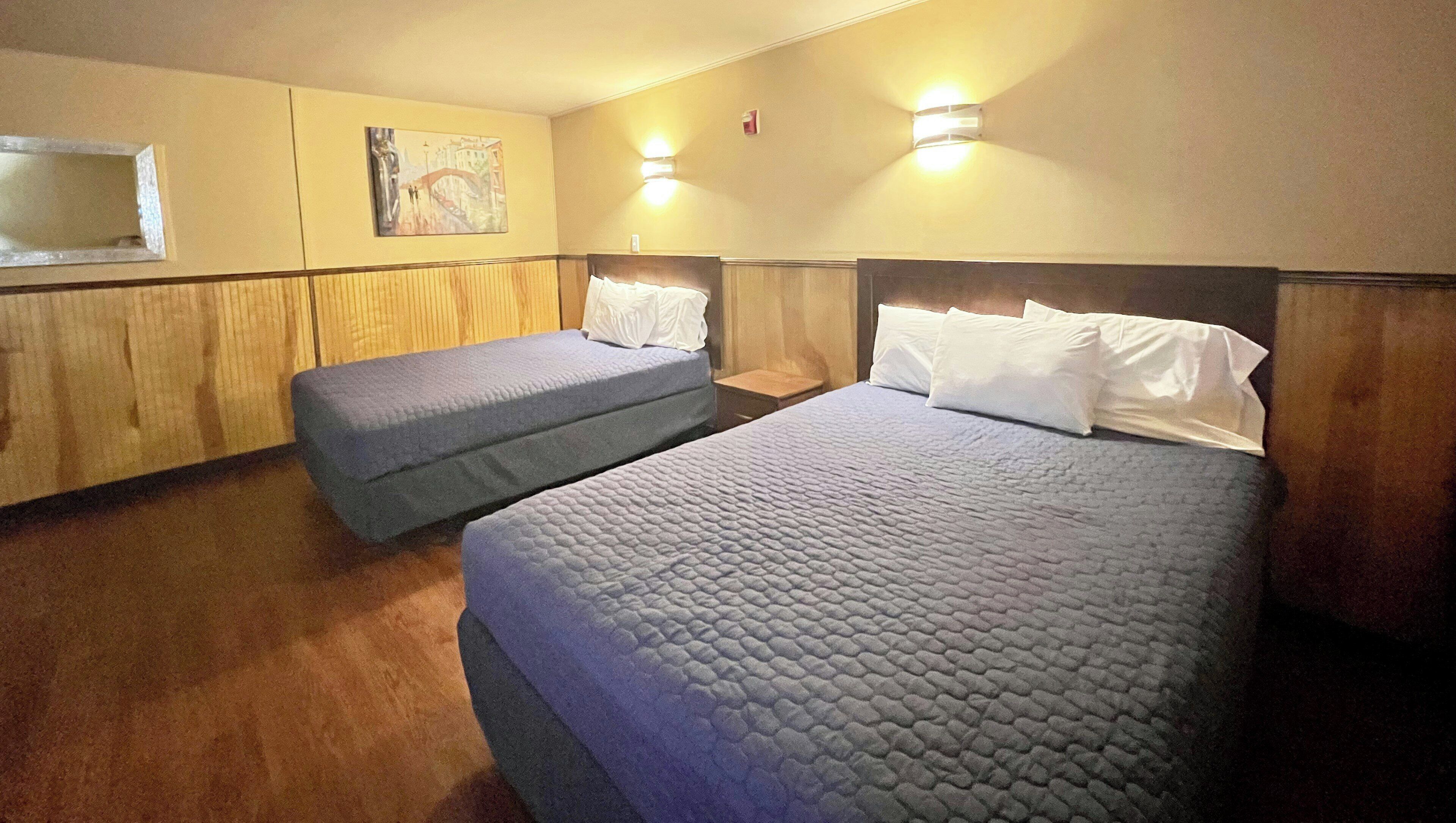 A hotel room with two beds, a wooden headboard, a painting on the wall, and a small table.