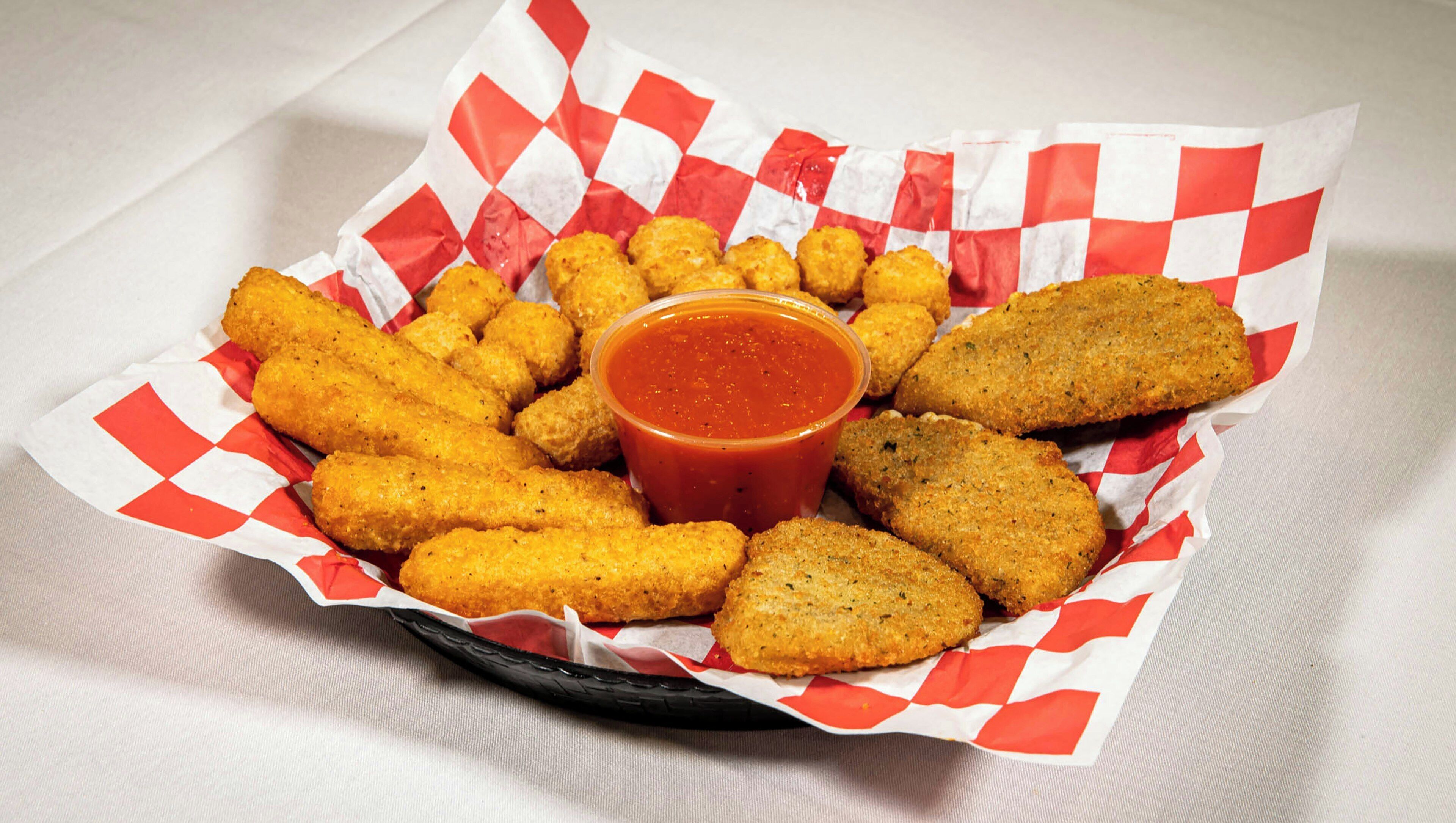 A basket of fried food items with a side of dipping sauce.