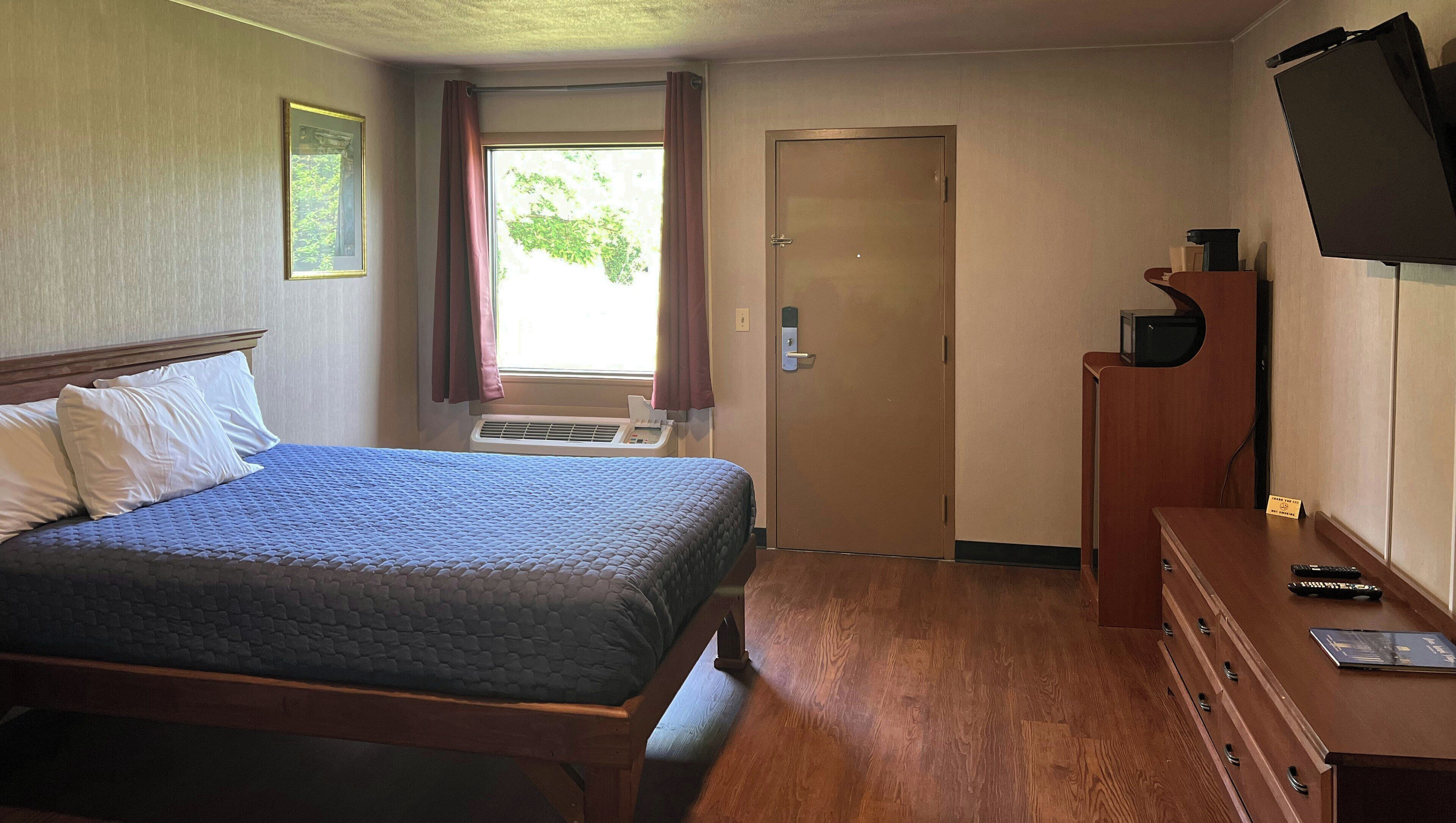 A hotel room with a bed, a desk, a television, and a door.