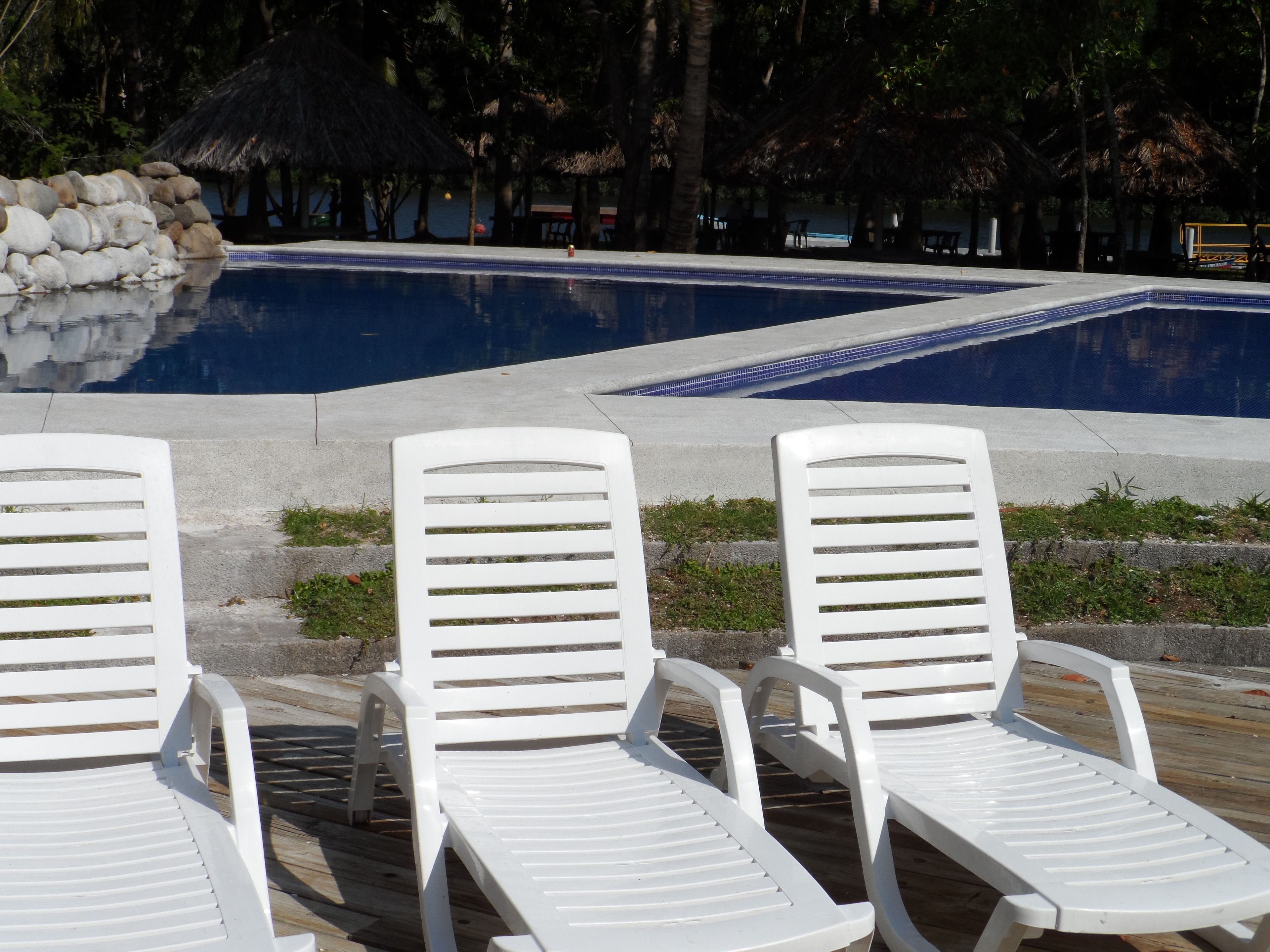 A pool area with two white lounge chairs and a stone wall.