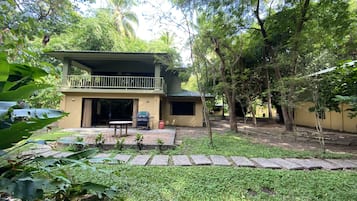 A two-story building with a balcony, surrounded by lush greenery and trees.