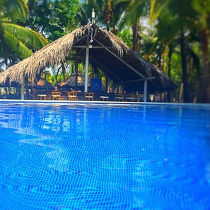 Una piscina con una estructura de techo de paja y sillas de fondo.