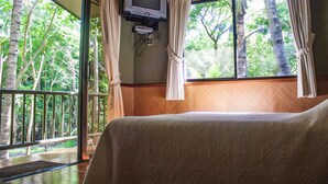 A room with a bed, a TV mounted on the wall, and a view of trees through the window. - Puerto Barillas Marina & Lodge (Usulutan)