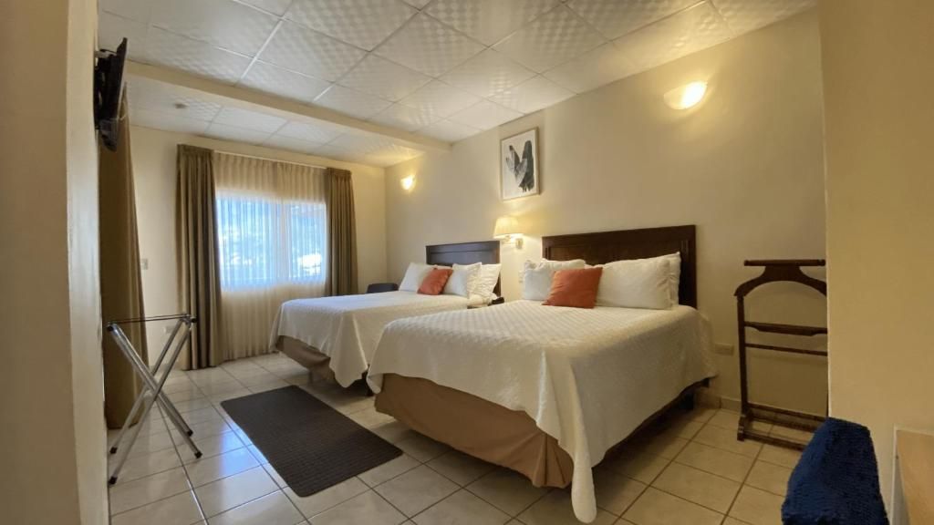 A hotel room with two beds, a flat-screen TV, a window with curtains, and a wall-mounted light fixture.