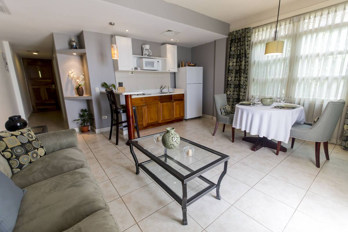 A modern living room with a glass coffee table, a sofa, and a dining area with a table set for two.